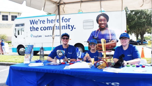 Community-Driven Health System A group of people sitting at a booth outside of a BayCare facility for a community event.