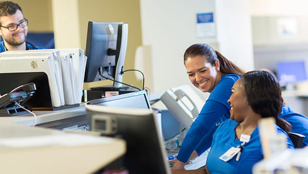Three BayCare nurses are talking at the nurses station on a patient floor.