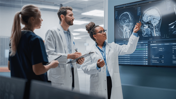 Three medical professionals reviewing an X-ray image displayed on a large screen during a graduate program session.