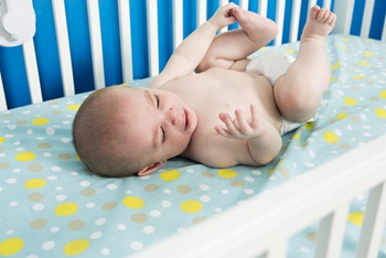 A cute one month old newborn baby is laying on her back in the crib crying