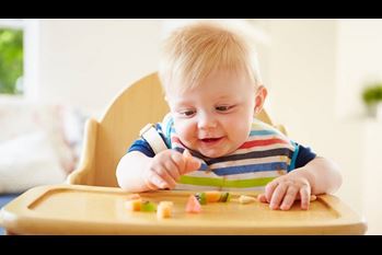 Baby Boy Eating Fruit In High Chair