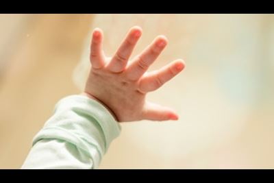 A baby puts her hand on window glass.