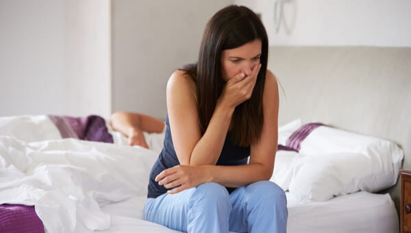 woman sitting on her bed covering her mouth