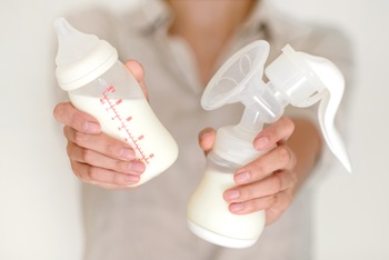 Breast pump and bottle with milk in womans hand in blurred background