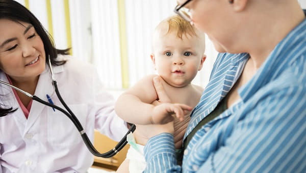 Cute Baby Being Examined By Doctor While Carrying By Mother