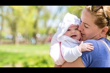 Cute baby in her mother's arms outdoors
