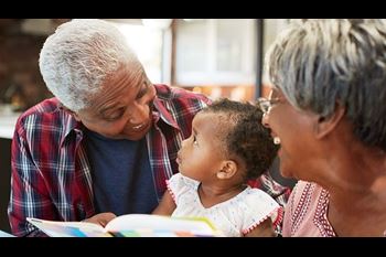 Grandparents Reading Book With Baby Granddaughter At Home