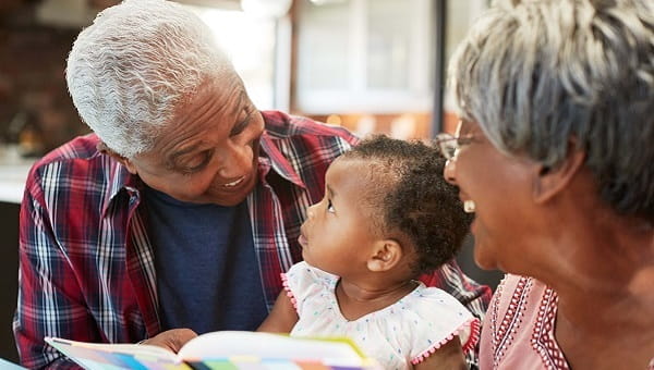 Grandparents Reading Book With Baby Granddaughter At Home
