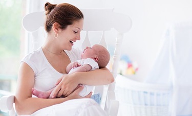 A new mom holds her baby while sitting in a rocking chair.