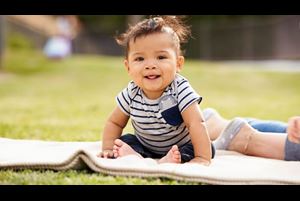 Little baby boy sitting up on a blanket in the park