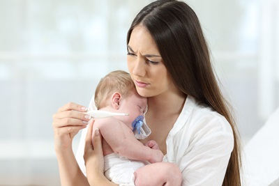 Mother checking thermometer holding her ill baby at home