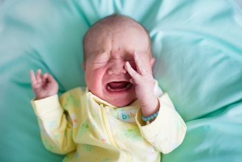 Newborn baby boy in bed on a green blanket crying