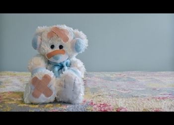 A white bear wearing blue earmuffs and scarf with adhesive bandages on its body