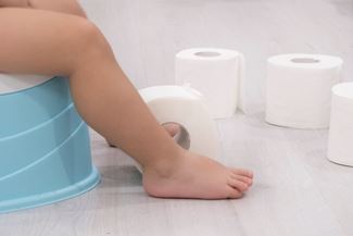 smiling baby sitting on chamber pot with toilet paper rolls