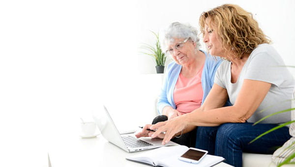 Senior lady sitting with caregiver in front of a laptop