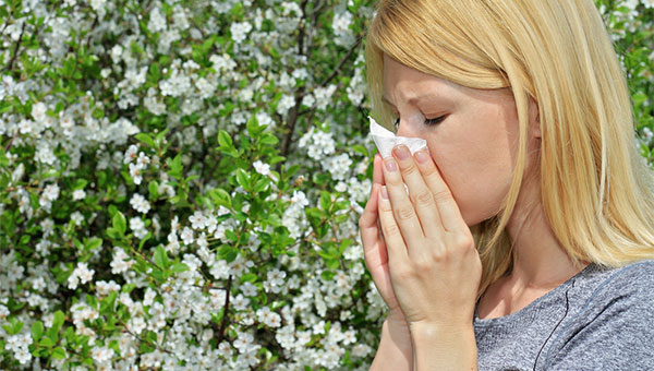 A woman using a tissue near a garden of flowers