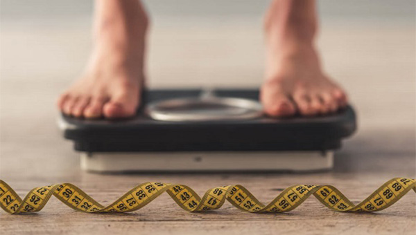 A person is standing on a scale, and a tape measure is on the floor.