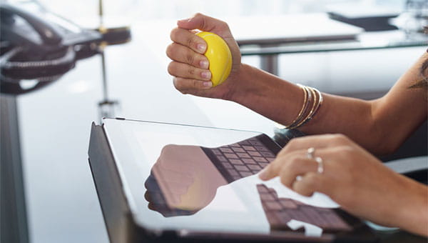 A woman is squeezing a stress ball while sitting in front of her computer