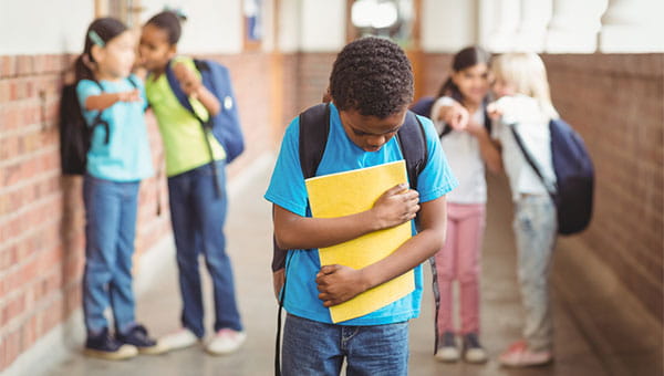 A boy walks through his school hallway while his classmates point at him and tease him