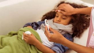 A mother has her hand on her daughter's forehead while checking her temperature on a thermometer.