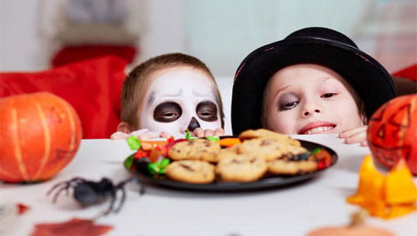Two children dressed up in Halloween costumes looking at cookies
