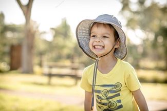 A little boy is wearing a large hat to protect his face from the sun.