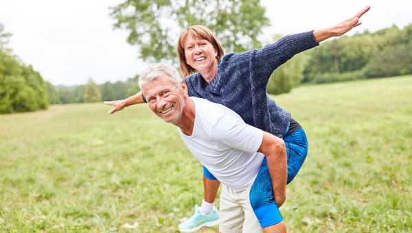 Senior woman rides piggyback on her partner's back in the park in summer