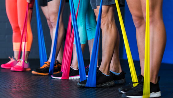 Low section of athletes exercising with resistance band in gym