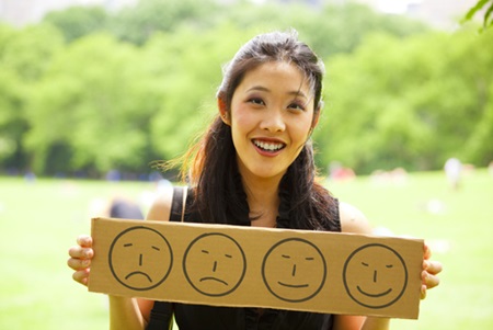 A woman is holding up a sign that has happy and sad faces on it