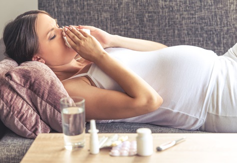 Pregnant woman laying on a couch with a tissue to her noses.