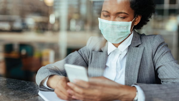 Black businesswoman wearing protective mask on her face while using smart phone and reading text message