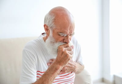 A senior man is coughing while holding his chest