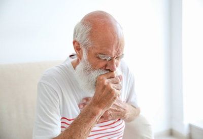 A senior man is coughing while holding his chest