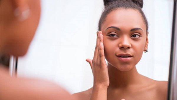 A young woman is looking in the mirror and putting lotion on her face