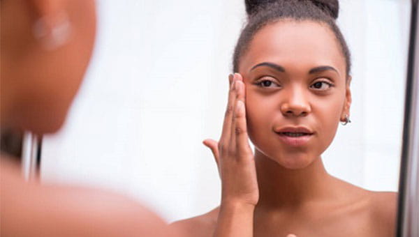 A young woman is looking in the mirror and putting lotion on her face