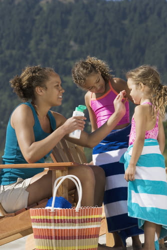 A woman puts sunscreen on her two young daughters