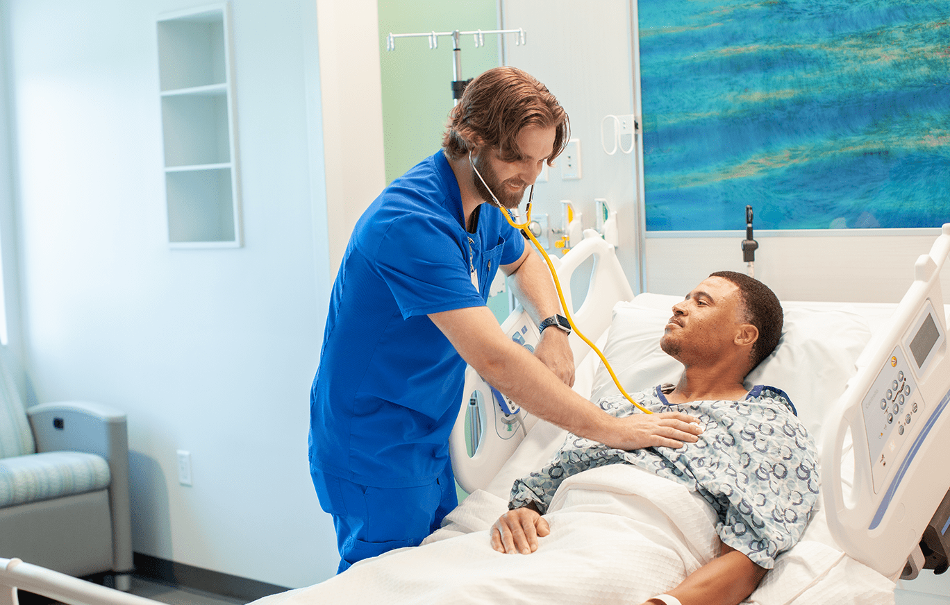 BayCare's Registered Nurse Residency Program A BayCare nurse in a bright patient room checking a patient heart beat with a stethoscope.