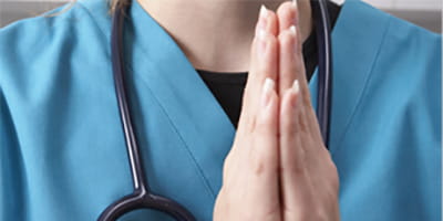A woman prays wearing hospital scrubs and a stethoscope around her neck