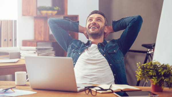 Happy young man working on laptop while sitting at his working place in office
