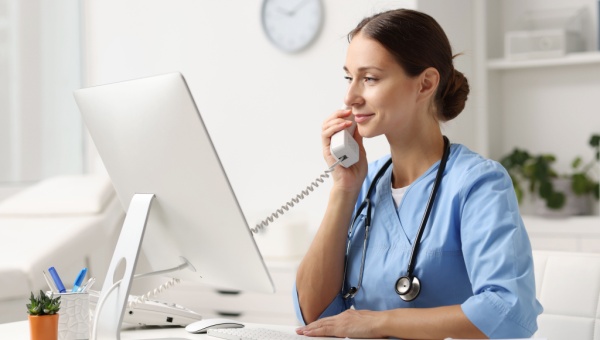 A nurse talks on the phone while looking at a computer screen.