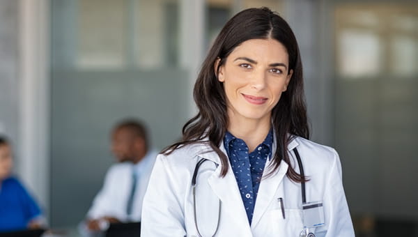 A female oncologist in a white coat stands before a group.