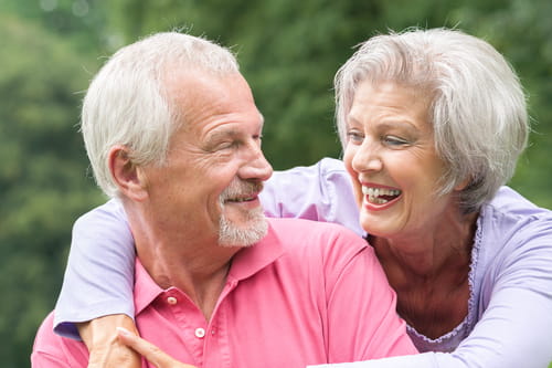 A senior couple looking at each other with the woman hugging the man
