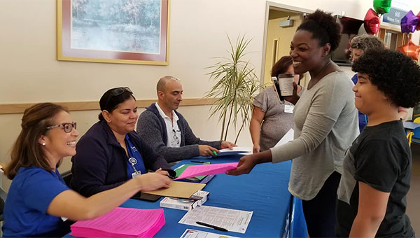 One male and two female BayCare volunteers are talking to people at a registration table.