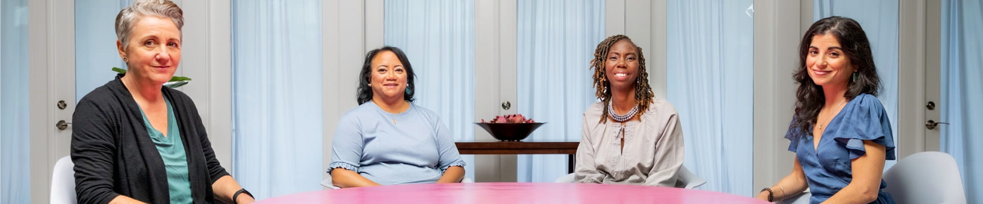 four women sitting at a round pink table