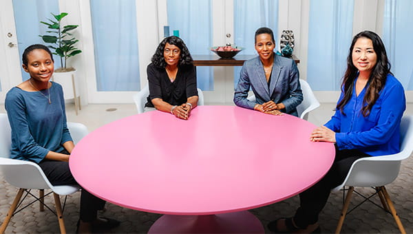 four ladies sitting around a pink table talking