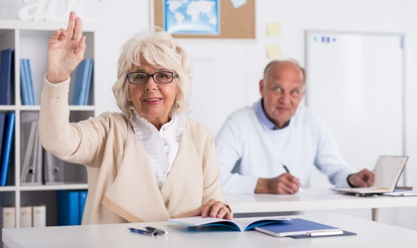 older woman and man in classroom with pens and notebooks