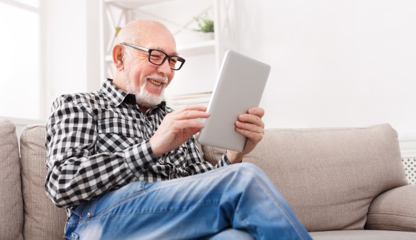 Senior man sitting on a couch reading emails on a tablet.