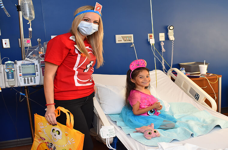 A child in a hospital bed with a person in costume next to the bed