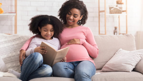 pregnant mother smiling with her daughter on the couch