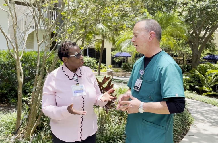 Female chaplain and male nurse are facing each other, having a heart-to-heart while walking down a sidewalk outside of St. Joseph's Hospital.